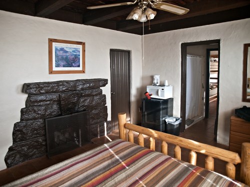 Cozy room featuring a wooden bed, stone fireplace, microwave, and a doorway leading to a bathroom.