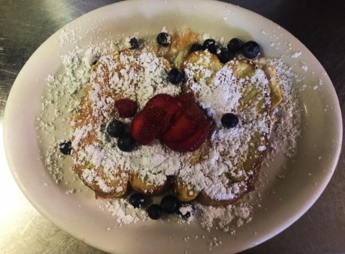 A plate of French toast topped with powdered sugar, strawberries, and blueberries.