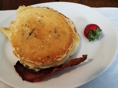 A plate with a golden pancake, crispy bacon, and a fresh strawberry on the side.