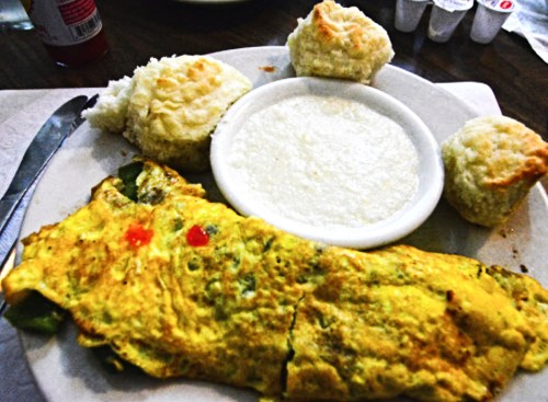 A plate with a vegetable omelet, grits in a bowl, and two fluffy biscuits.