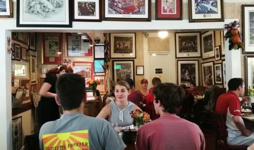 A busy restaurant with framed photos on the walls, featuring diners at tables and a server in the background.
