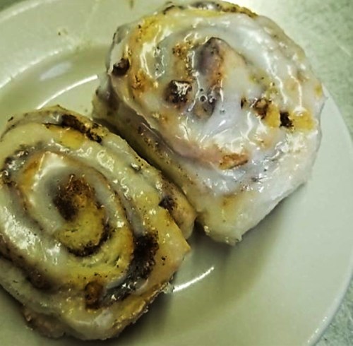 Two cinnamon rolls with a glossy icing on a white plate, showcasing their swirled layers and golden-brown edges.