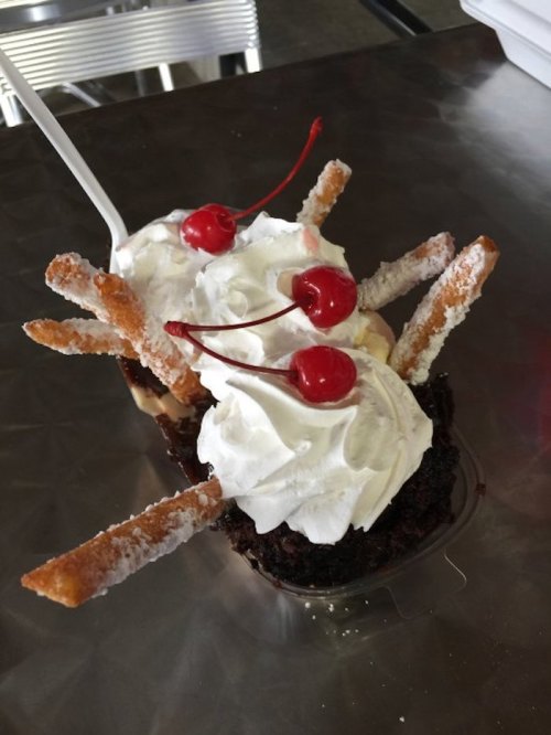 A dessert featuring two scoops of ice cream topped with whipped cream and cherries, served with crispy sticks.