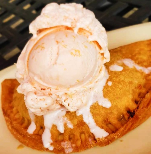 A warm, golden pastry topped with melting ice cream, drizzled with cream, on a white plate.