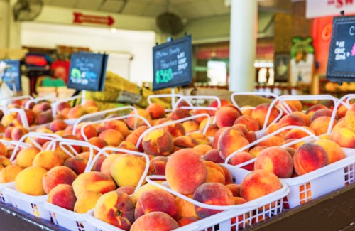 Baskets of fresh peaches displayed at a market, with price signs visible in the background.