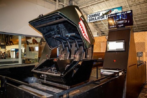 A combat flight simulator with a cockpit design, featuring controls and a screen displaying flight information.