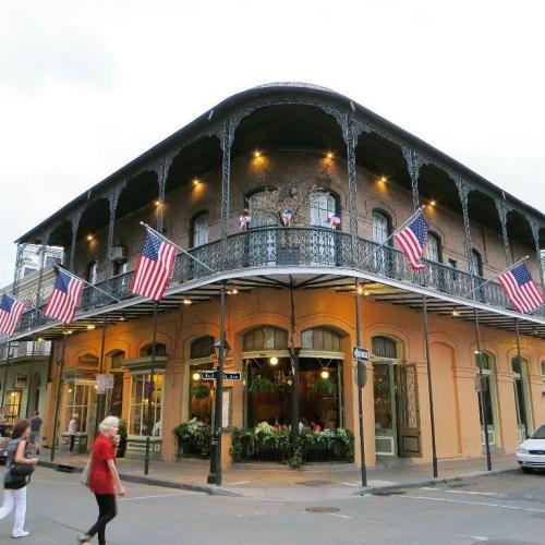 Historic building with wrought iron balconies, American flags, and people walking in a lively street scene.