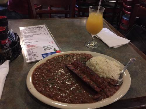 A plate of rice and beans with sausage, accompanied by a glass of orange drink and a menu on a table.