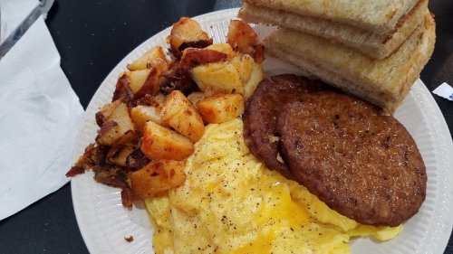A plate of breakfast featuring scrambled eggs, sausage patties, seasoned potatoes, and toasted bread.