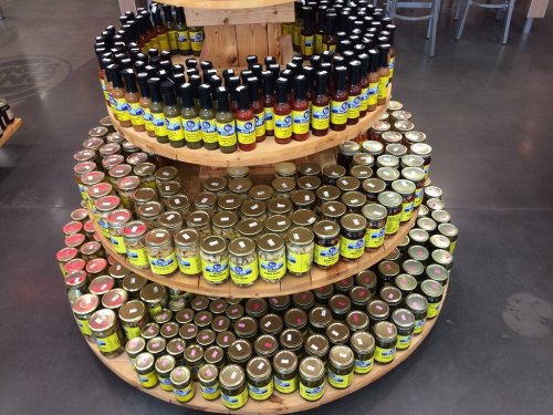 A wooden display stand with multiple tiers, showcasing jars and bottles of various sauces and condiments.