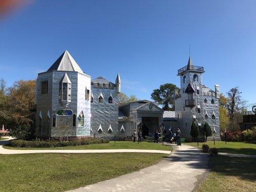 A whimsical castle covered in shiny silver material, surrounded by greenery and visitors on a sunny day.