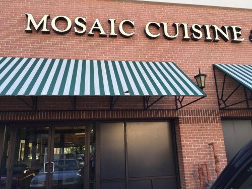 Exterior of a restaurant named "Mosaic Cuisine," featuring green and white striped awnings and a brick facade.