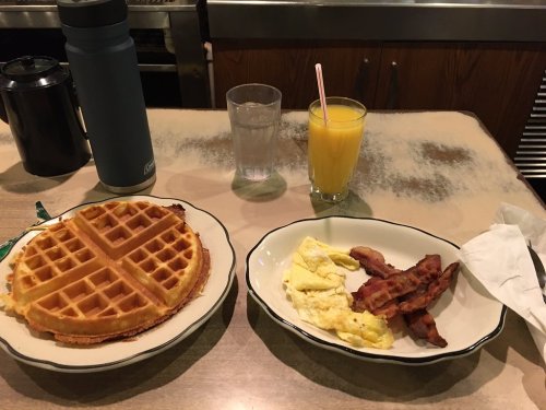 A plate with a waffle, scrambled eggs, and bacon, alongside a glass of orange juice and a water glass.