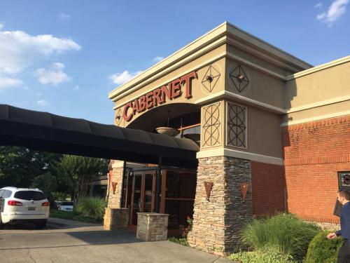 Exterior of a restaurant named "Cabernet," featuring a stone facade and a covered entrance under a blue sky.