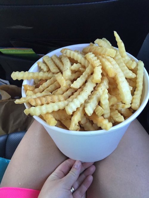 A large white container filled with crinkle-cut fries, resting on a person's lap in a car.