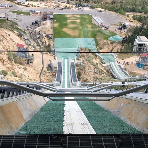 View from the top of a ski jump, showing the landing area and surrounding landscape.