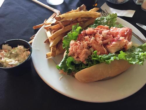 A plate featuring a lobster roll on lettuce, served with fries and a side of coleslaw.