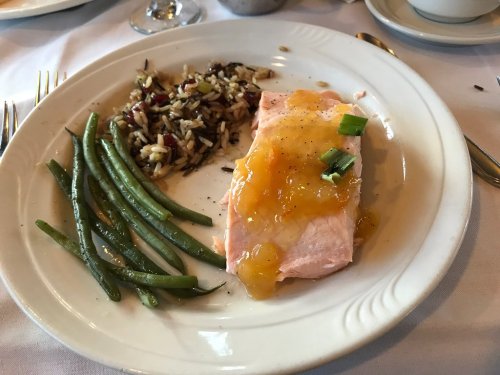 A plate with salmon topped with sauce, served with green beans and a side of wild rice.