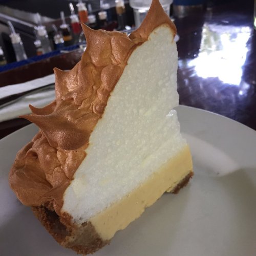 A slice of pie with a golden meringue topping, creamy filling, and a crumbly crust on a white plate.