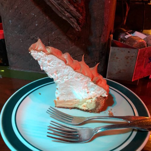 A slice of pie with a fluffy meringue topping on a plate, accompanied by two forks.