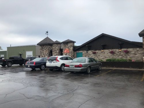 A parking lot with several cars in front of a stone and wood building under a cloudy sky.