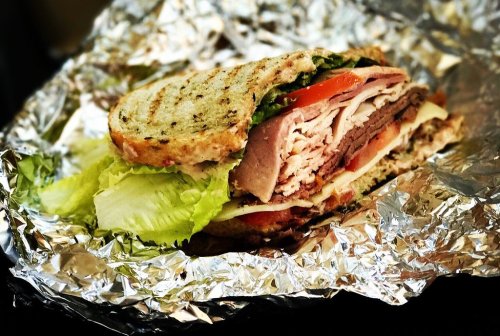 A delicious sandwich with layers of turkey, ham, lettuce, and tomato, wrapped in foil.