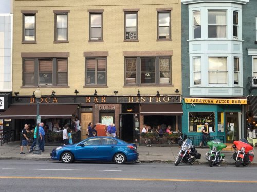 A street view of Boca Bar Bistrot and Saratoga Juice Bar, with people walking and dining outside.