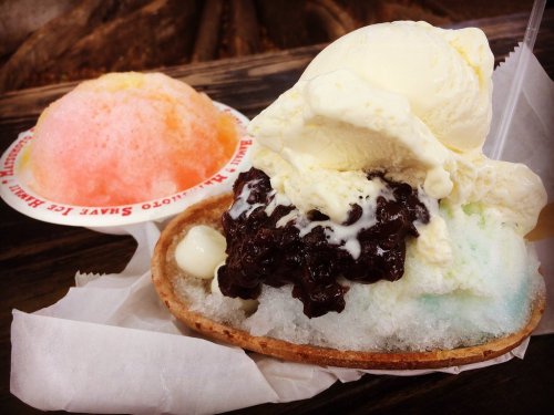 A colorful dessert featuring shaved ice topped with syrup and a scoop of vanilla ice cream on a cookie-like base.