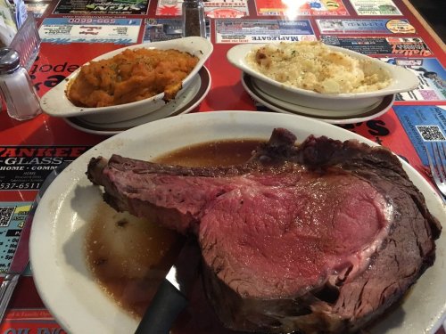 A large prime rib on a plate with sides of mashed sweet potatoes and macaroni and cheese on a colorful table.