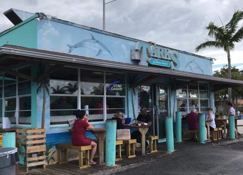 A colorful seafood restaurant with a dolphin mural, featuring outdoor seating and patrons enjoying their meals.