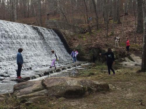 People exploring a waterfall area, walking on rocks and enjoying nature in a wooded setting.
