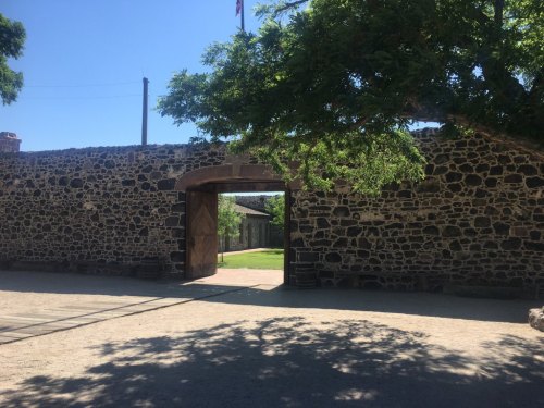 A stone wall with a wooden gate, framed by trees, under a clear blue sky.