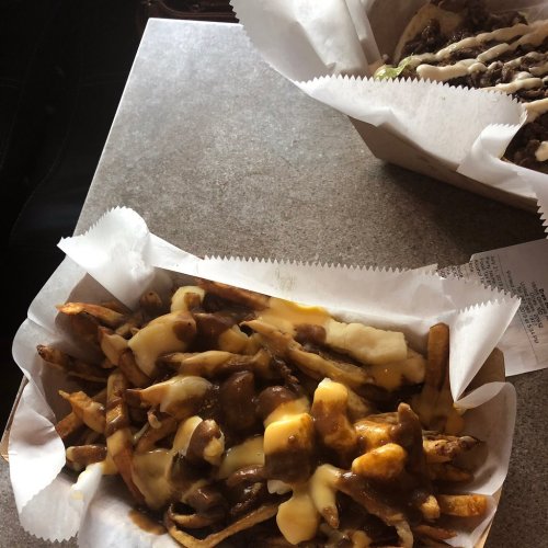 A serving of loaded fries topped with cheese and gravy, placed on a table with another dish in the background.
