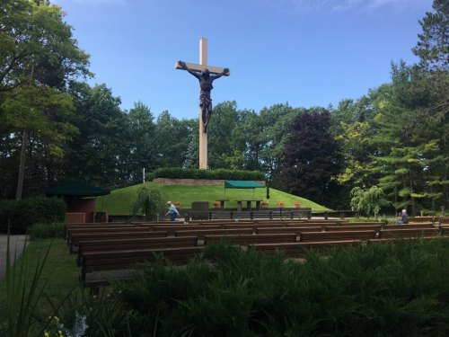 Outdoor religious site featuring a large crucifix on a hill, surrounded by benches and trees under a clear blue sky.