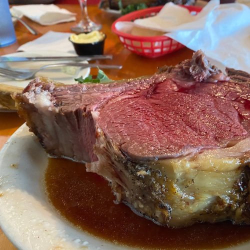 A large, juicy slice of prime rib on a plate, surrounded by a rich brown sauce.