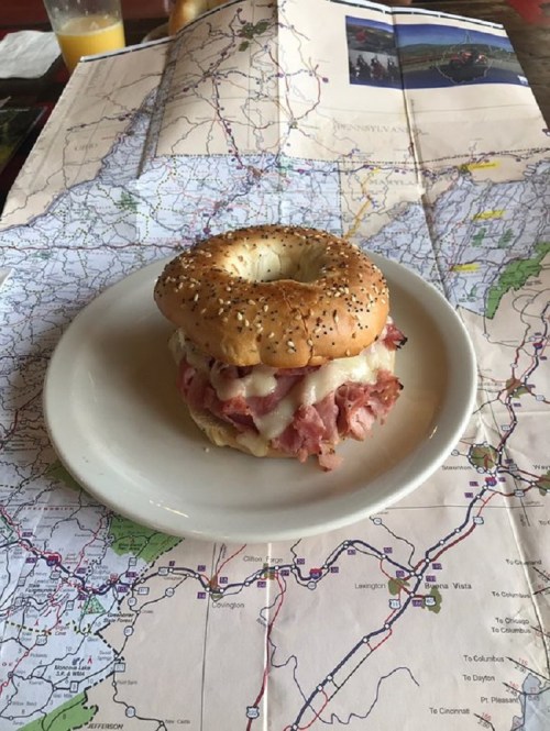 A bagel sandwich with ham and cheese on a plate, placed on top of a detailed map.