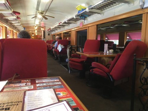Interior of a diner with red upholstered chairs and tables, featuring a train-themed decor and a cozy atmosphere.
