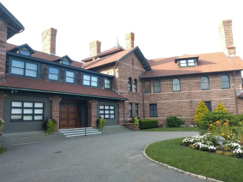 Historic stone mansion with a landscaped garden, featuring multiple chimneys and a welcoming entrance.