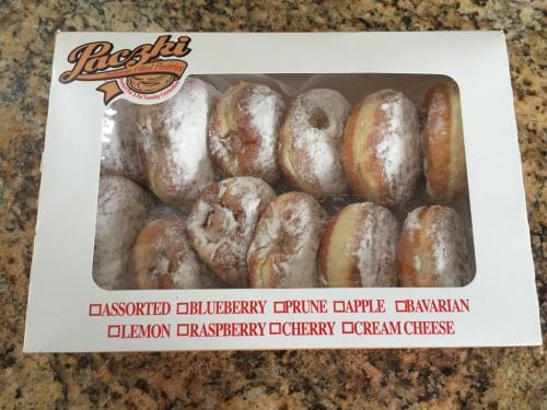 A box of assorted paczki donuts, featuring various flavors like blueberry, raspberry, and cream cheese, dusted with powdered sugar.