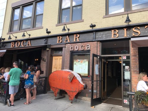 Exterior of Boca Bar Bistro with a large pig sculpture and people waiting outside.