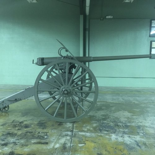A vintage cannon displayed indoors, featuring a large wheel and a long barrel, set against a green wall.
