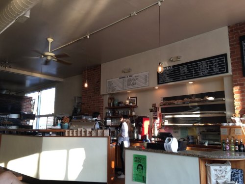 A cozy café interior with a counter, menu board, and staff serving customers in warm, natural light.