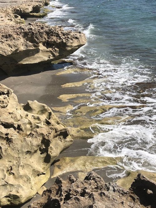 Rocky shoreline with gentle waves lapping against the sand and water, creating a serene coastal scene.