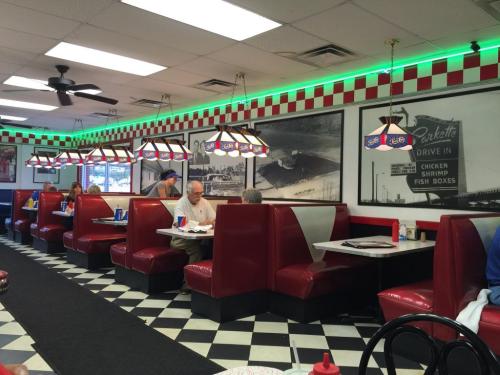 A retro diner interior with red booths, checkered floor, and vintage decor, featuring customers dining and chatting.