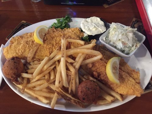A plate of fried fish fillets with lemon, served with fries, coleslaw, and dipping sauce.