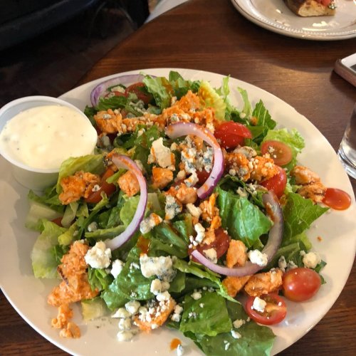 A fresh salad with greens, cherry tomatoes, red onions, blue cheese, and a side of ranch dressing.