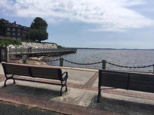 Two benches face a calm lake with a wooden pier in the background, under a partly cloudy sky.
