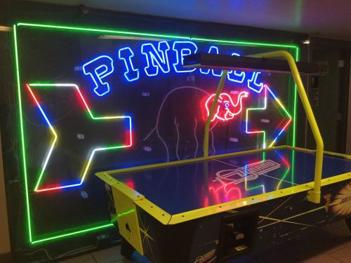 Neon sign reading "PINBALL" with an elephant graphic, illuminated behind an air hockey table.