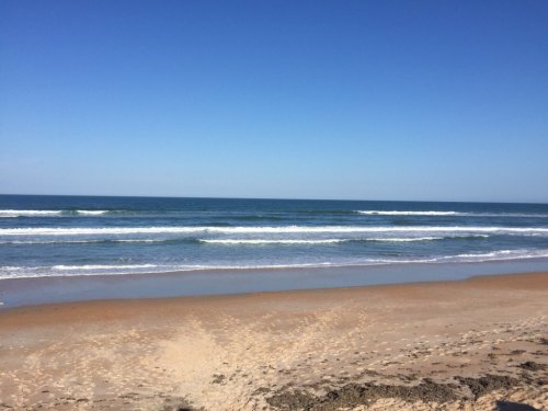 A serene beach scene with gentle waves, golden sand, and a clear blue sky.