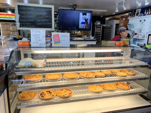A display case filled with various pies and baked goods, with a staff member in the background at a bakery.